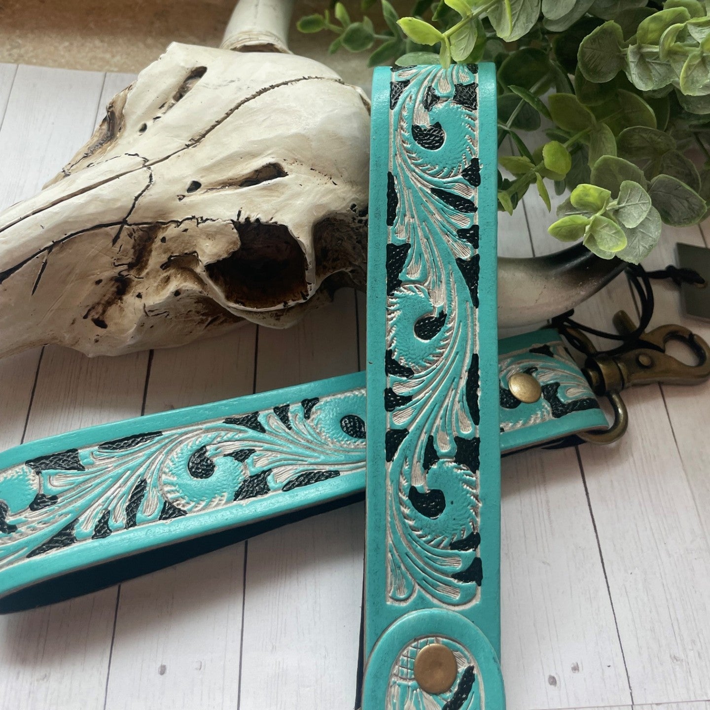 Turquoise decorative shelf with intricate patterns next to a cow skull and greenery on a wooden floor.