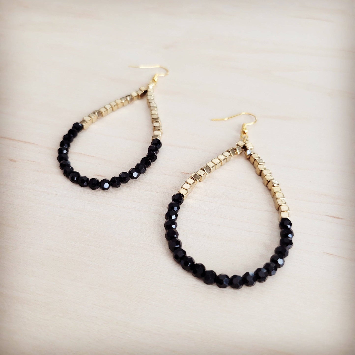Pair of black beaded earrings with gold accents on a light wooden surface