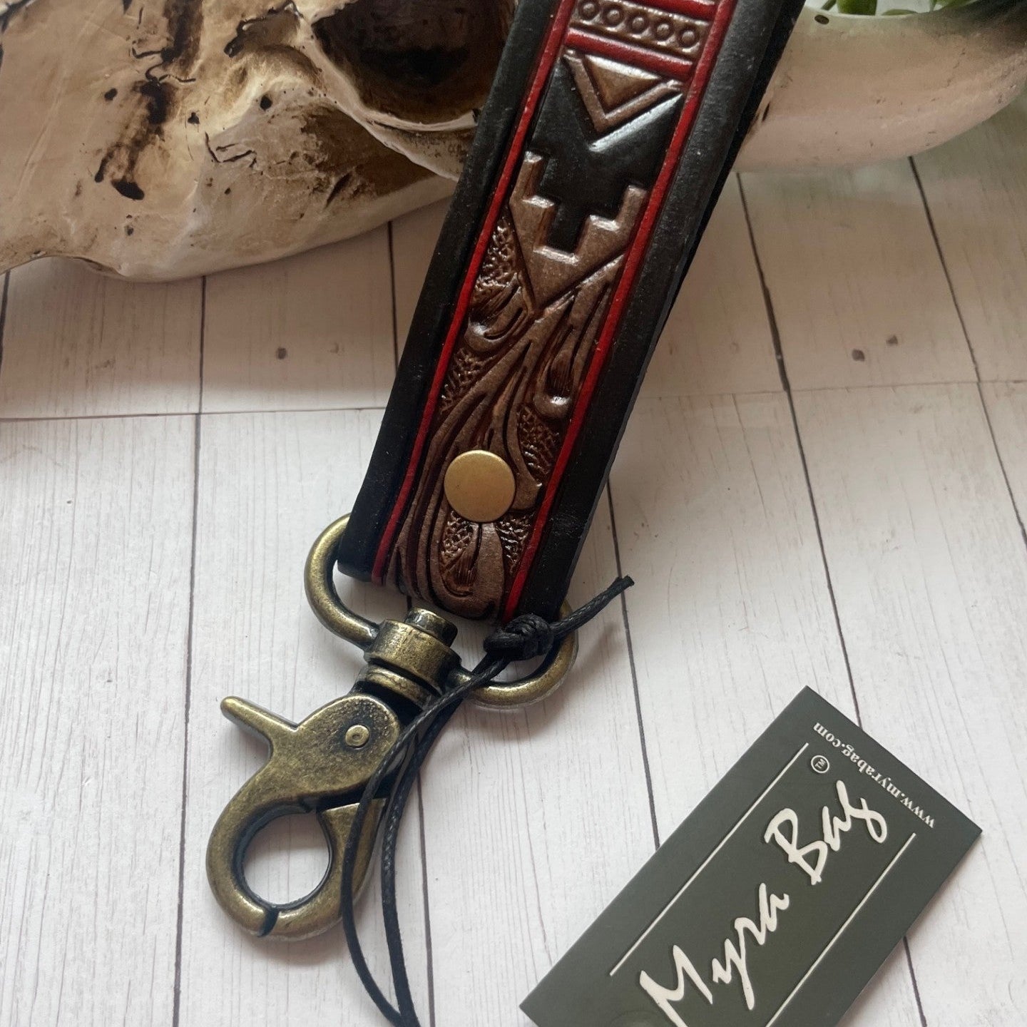Decorative leather keychain with intricate designs on a wooden surface, featuring a 'Myra Bex' tag.