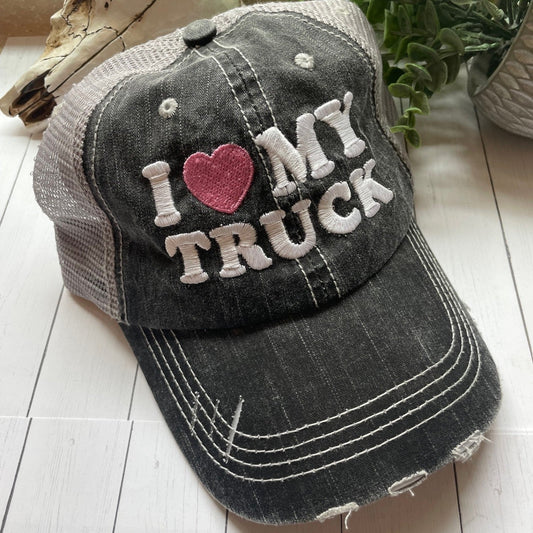 Black distressed baseball cap with 'I ❤️ MY TRUCK' text on a light wooden surface.