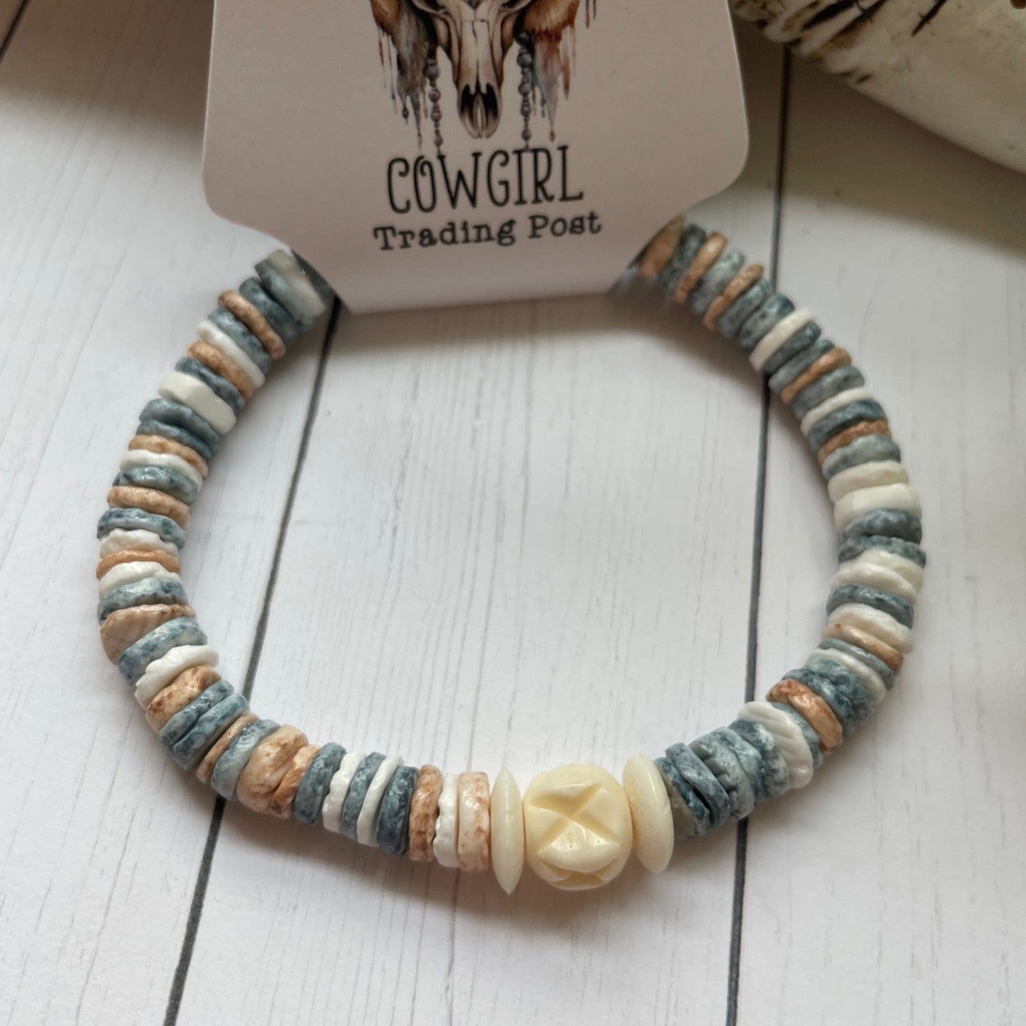 round pastel beads with a white bead accent on a white wooden surface, branded 'The Cowgirl Trading Post'.