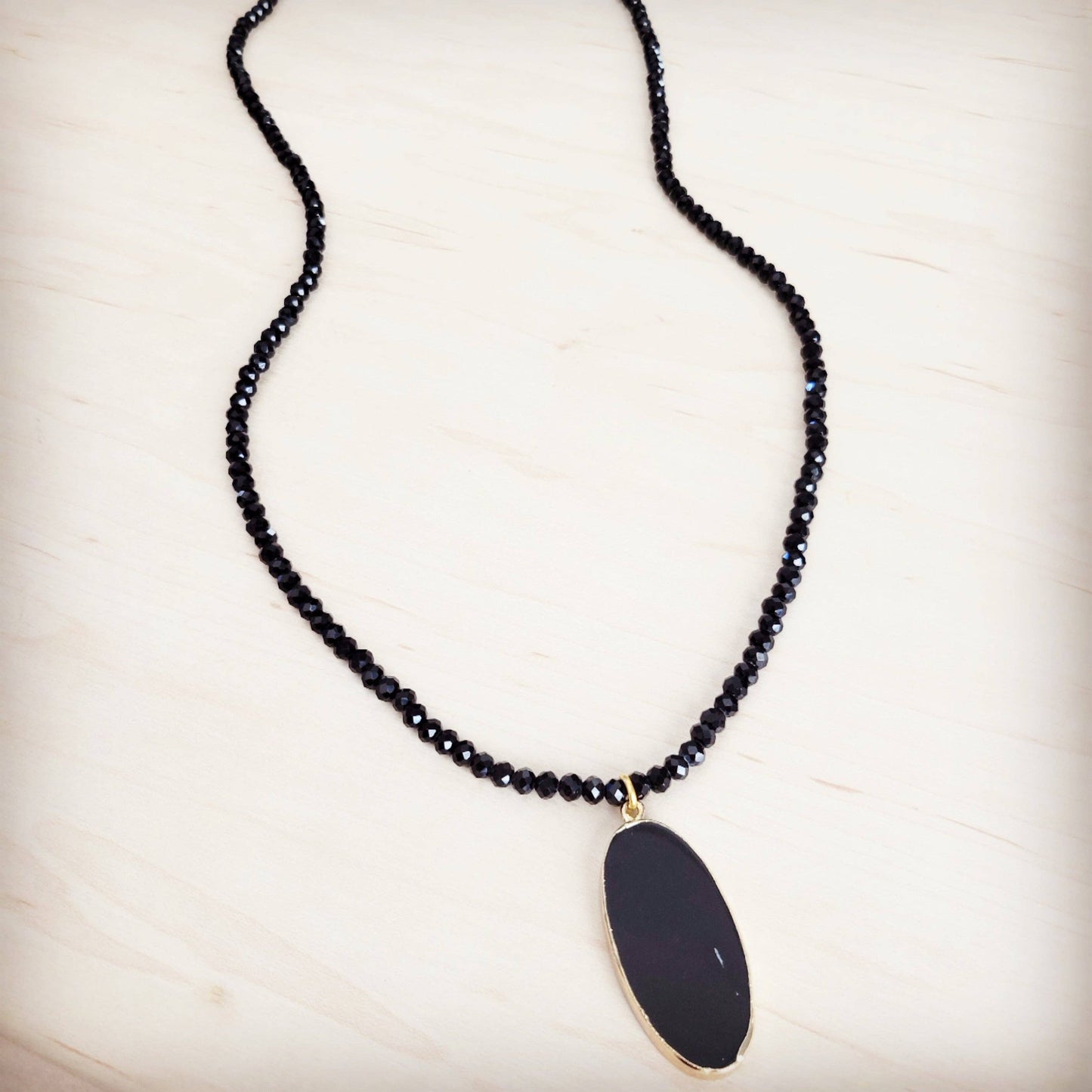Black beaded necklace with a large black pendant on a light background