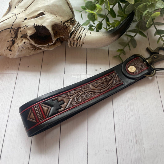 Decorative leather strap with intricate patterns on a light wooden surface with a skull and plant in the background.