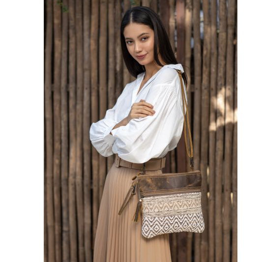 Woman holding a brown leather bag with intricate patterns against a wooden background