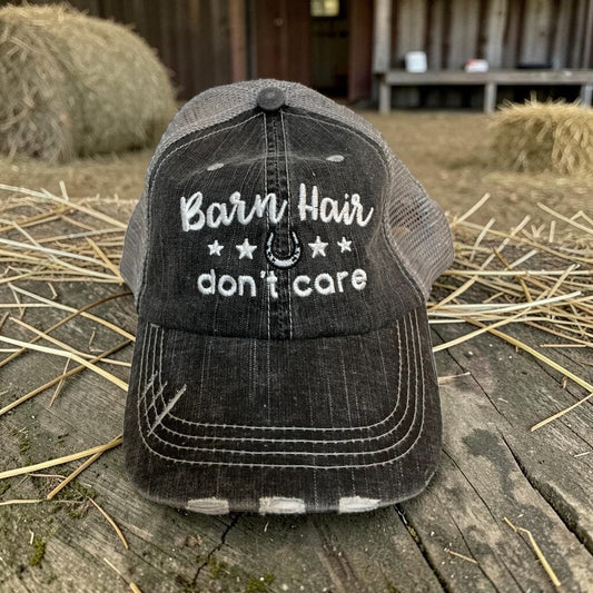 Black cap with 'Barn Hair don't care' text on a wooden surface with hay bales in the background