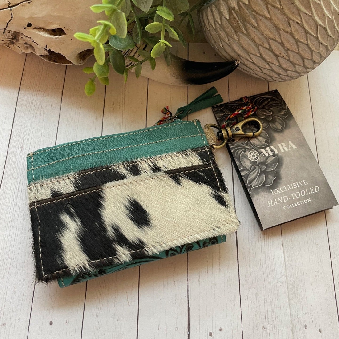 Cardholder with cowhide design and teal accents on a wooden surface with a plant in the background