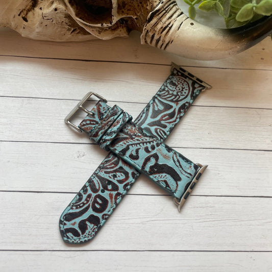 Teal and black patterned watch strap on a wooden surface with a skull and plant in the background