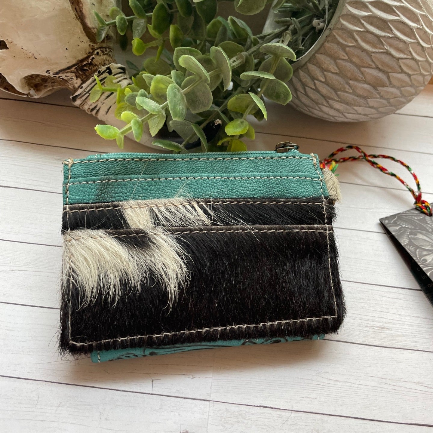Small wallet with black and white fur pattern on a light wooden surface with plants in the background