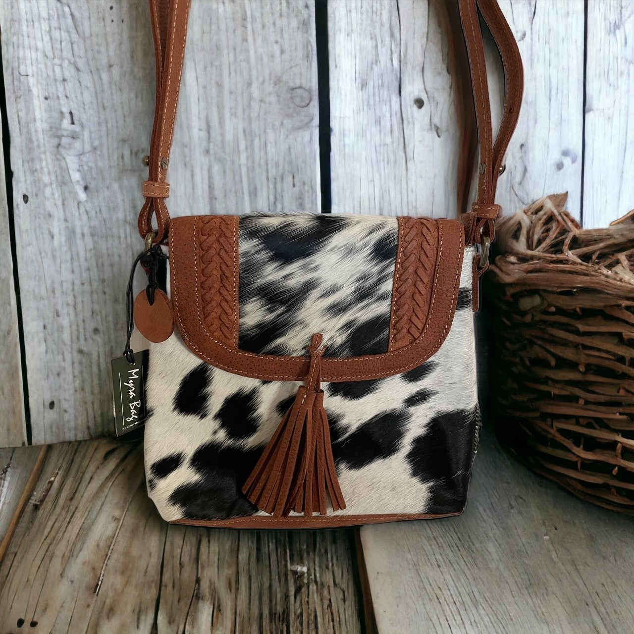 Cow print handbag with brown leather accents on a wooden surface