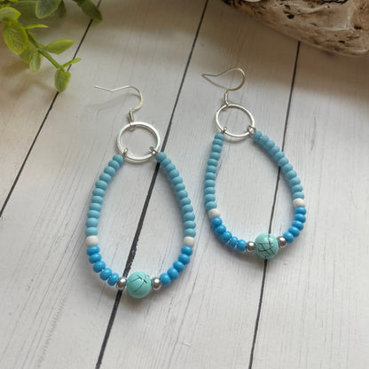 Turquoise beaded earrings on a wooden surface with natural elements.