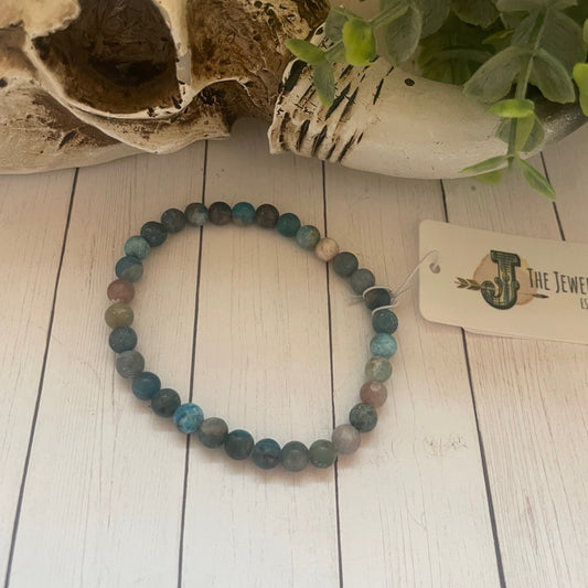 Multicolored beaded bracelet on a white wooden surface with a skull and plant in the background.
