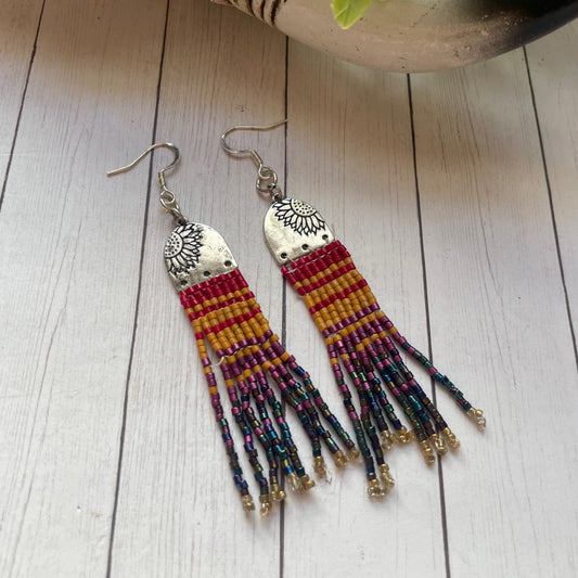 Colorful beaded earrings on a wooden surface with a plant in the background