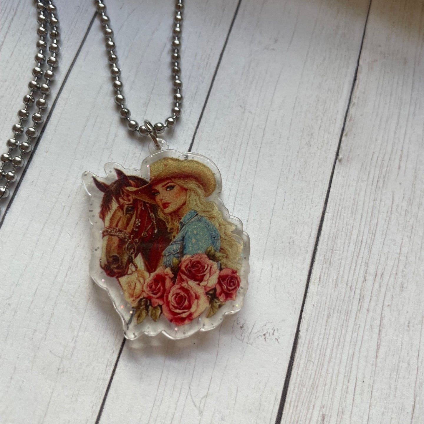 Necklace with a pendant featuring a woman, horse, and flowers on a wooden surface