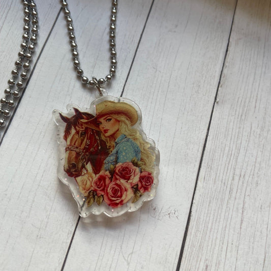 Necklace with a pendant featuring a woman, horse, and flowers on a wooden surface