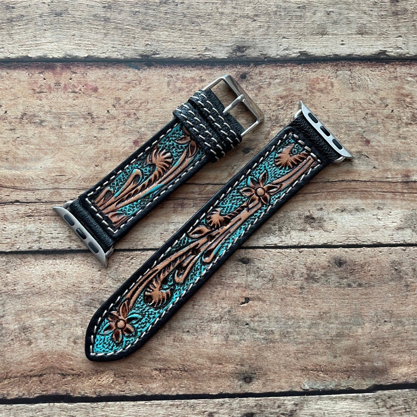 Two leather watch straps with intricate designs on a wooden surface