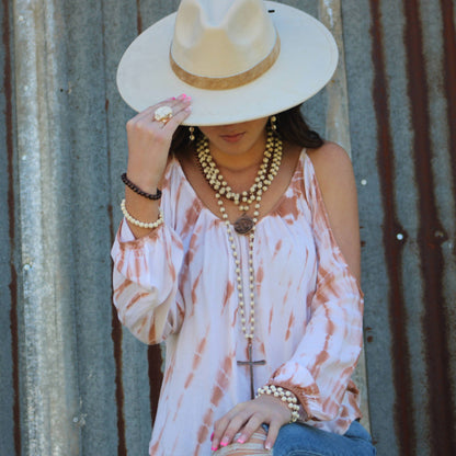 Woman wearing a wide-brimmed hat and layered necklaces against a corrugated metal background