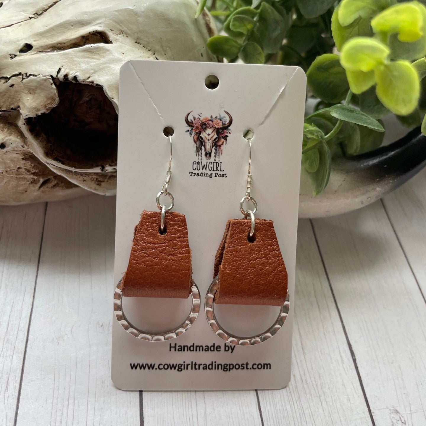 Brown leather earrings on a branded card with a rustic background