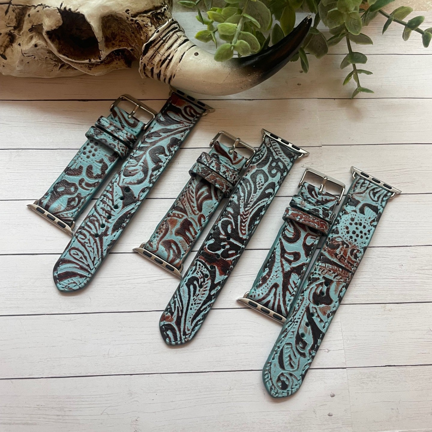 Set of patterned watch straps on a wooden surface with a skull and plant in the background