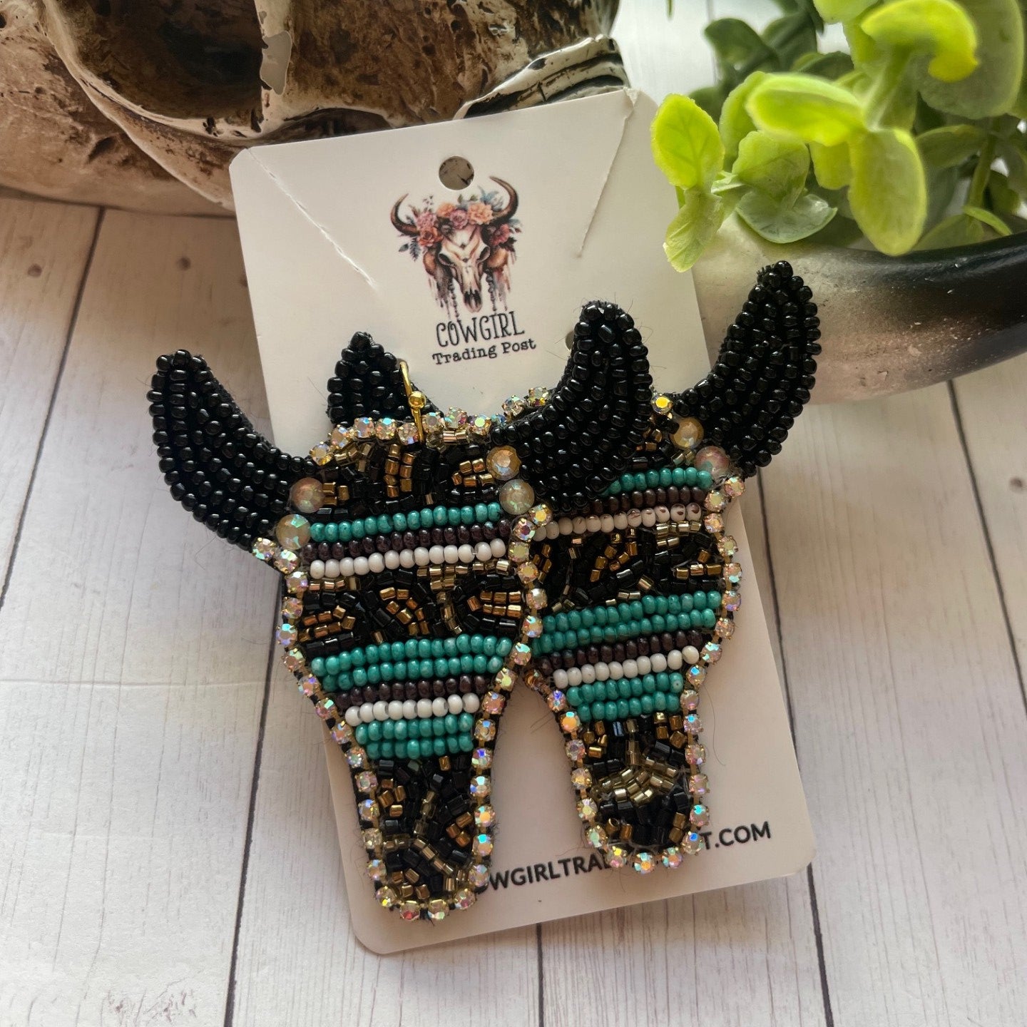 Beaded fish-shaped earrings on a card with a plant in the background