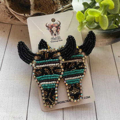 Beaded fish-shaped earrings on a card with a plant in the background