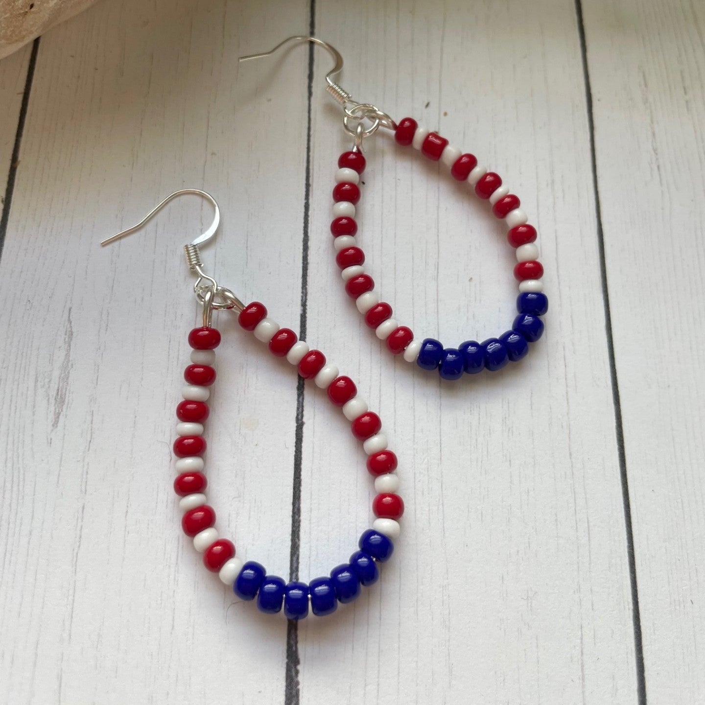 red white and blue teardrop shaped earrings in a teardrop shape on a white card with white wood background and a skull and greenery