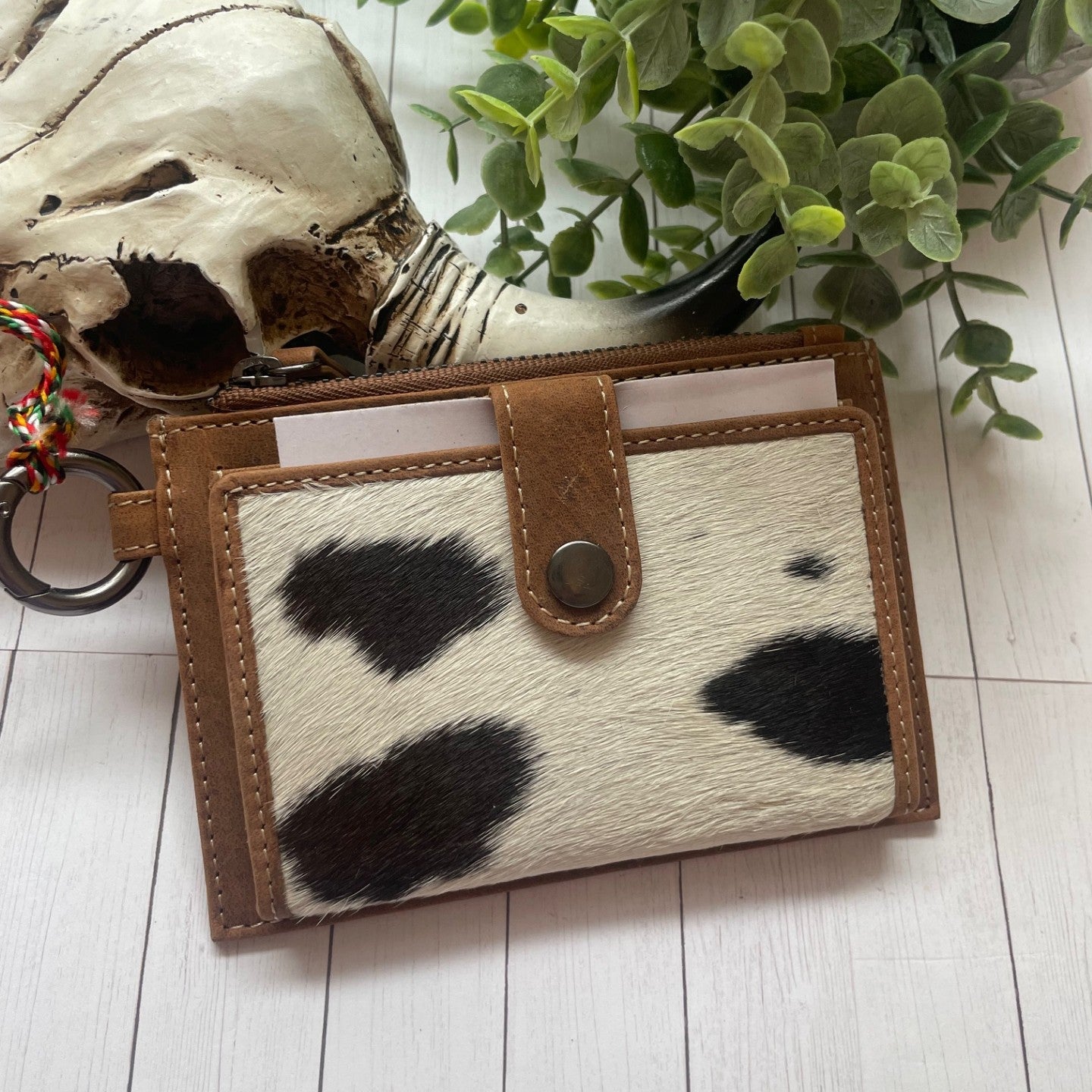 Cow print wallet with brown leather accents on a light wooden surface with a plant in the background