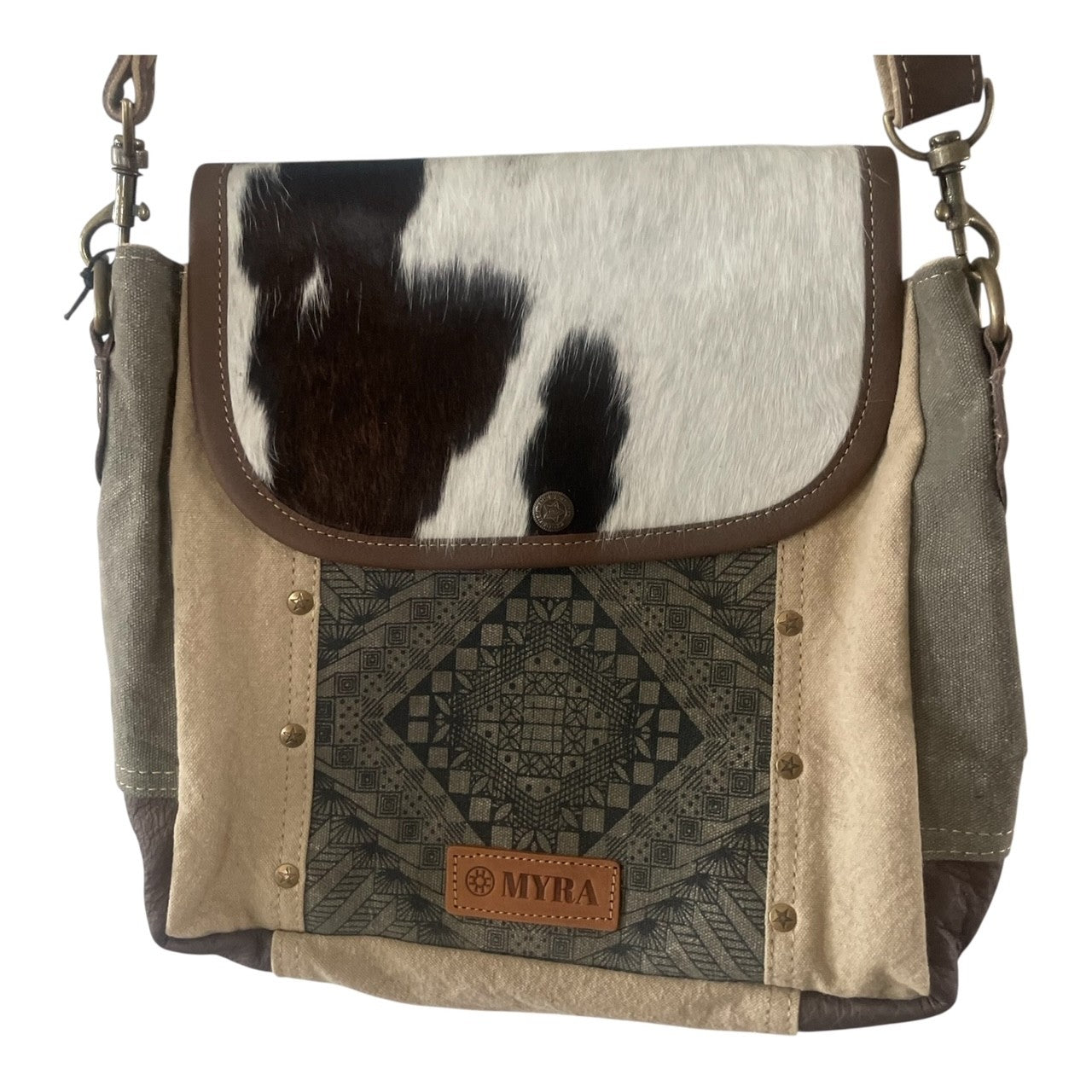 A bohemian-style shoulder bag featuring a cowhide flap, beige canvas panels, a geometric patterned front pocket, and a tan leather brand patch reading 'MYRA'.