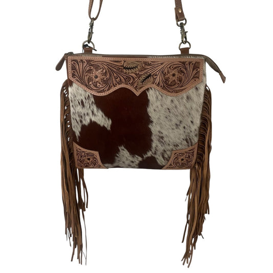 A western-style shoulder bag featuring a brown and white cowhide body, tooled brown leather trim, and long brown fringe, shown against a plain white background.