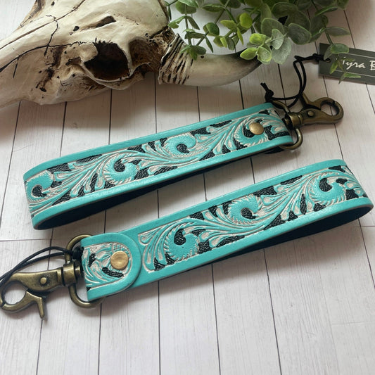 Turquoise leather strap with intricate designs on a white surface with a cow skull and plant.