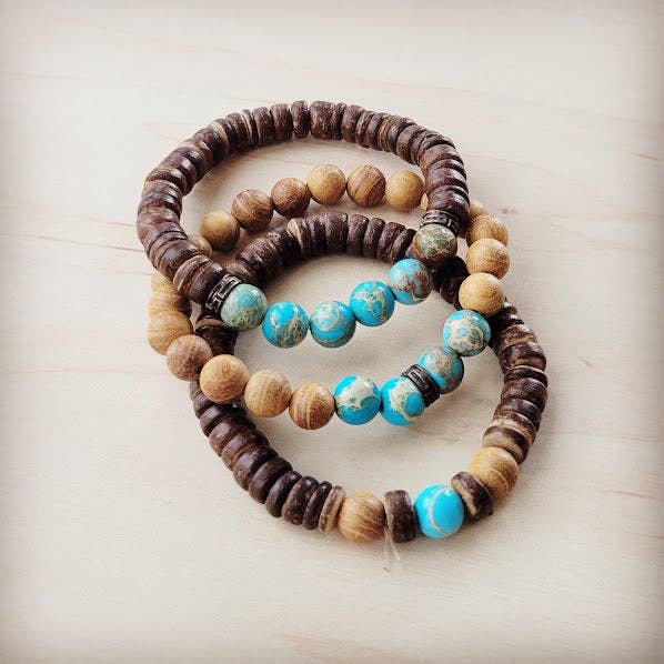Three beaded bracelets with brown, beige, and turquoise beads on a light wooden surface.