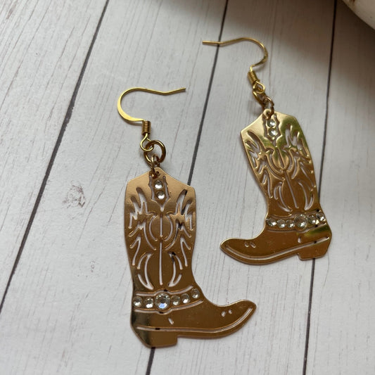 Gold Cowboy boot with sparkly stone earrings on a wooden surface