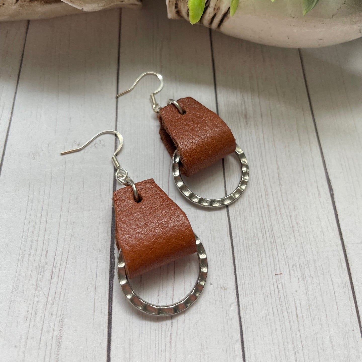 Brown leather strips holding a textured small ring earrings