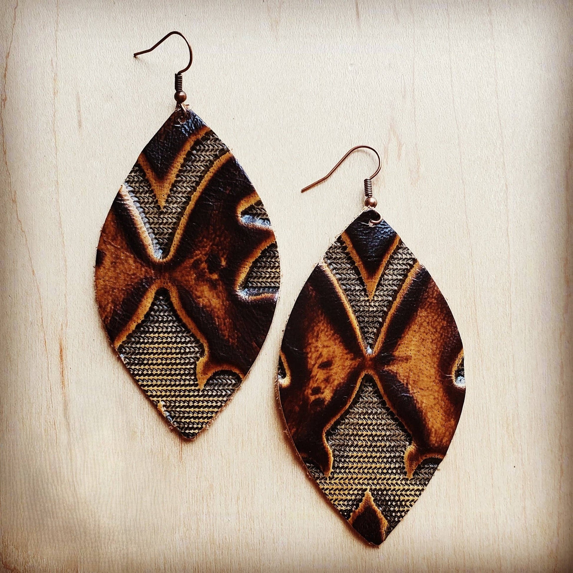 Pair of leaf-shaped earrings with a brown and gold pattern on a wooden surface.
