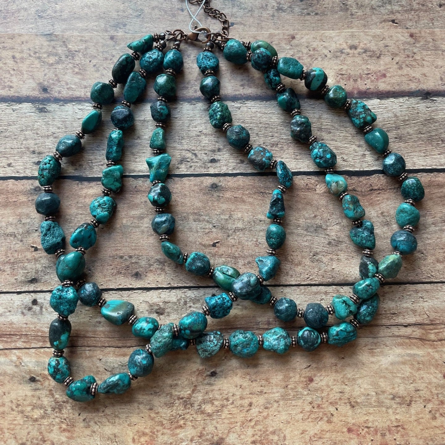 Turquoise beaded necklace on a wooden surface with a tag.