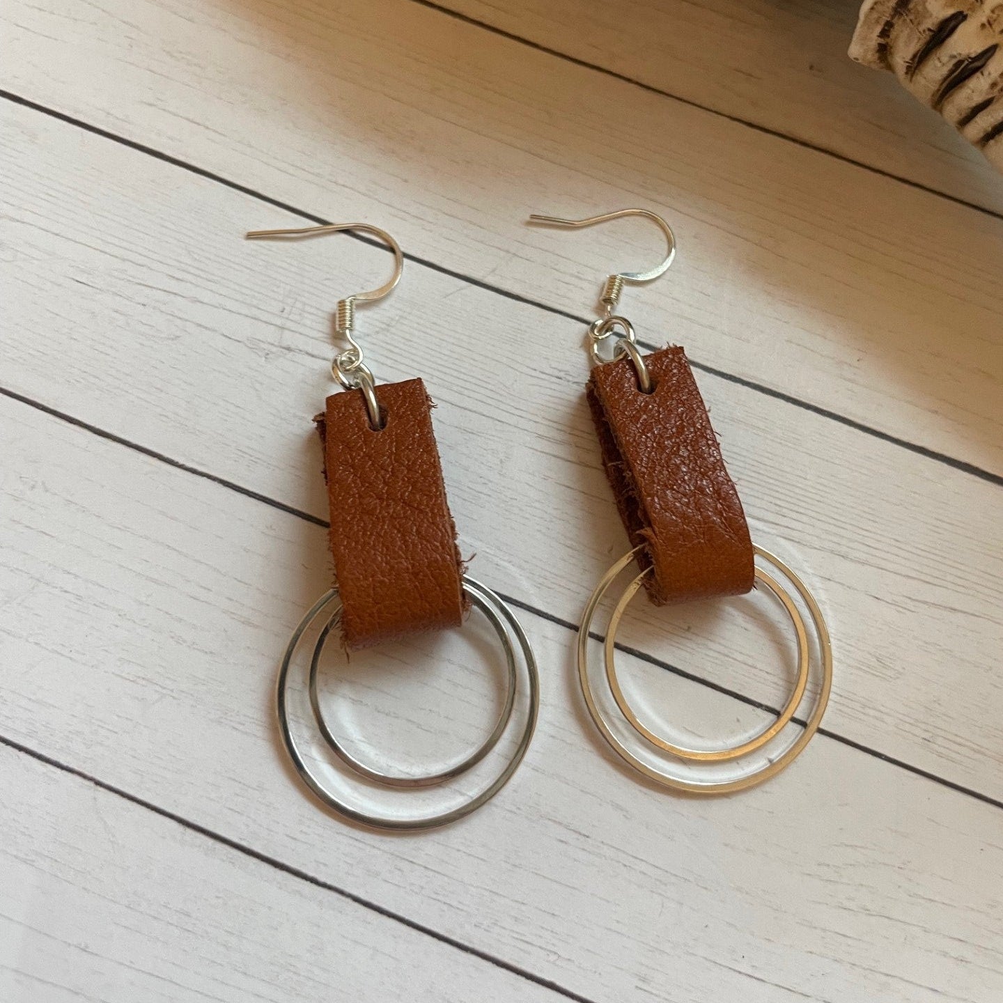 Pair of earrings with brown leather accents on a light wooden surface