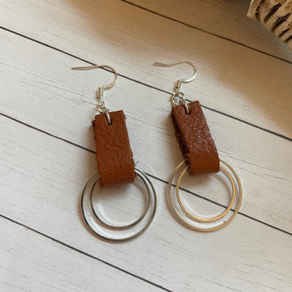 Pair of earrings with brown leather accents on a light wooden surface
