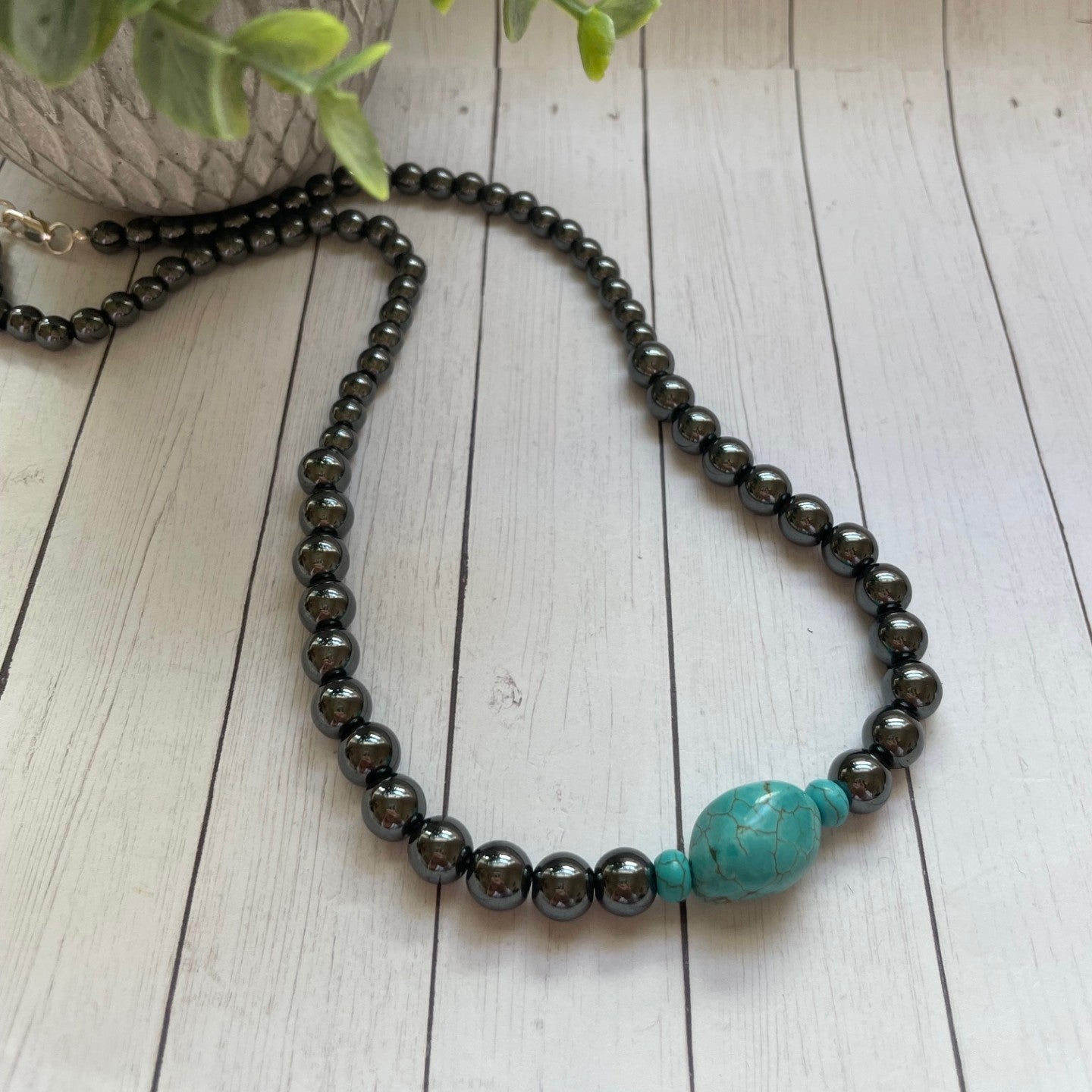 Necklace with black beads and a turquoise bead on a wooden surface