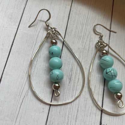 Three Turquoise beads inside a silver teardrop shape earrings on a wooden surface