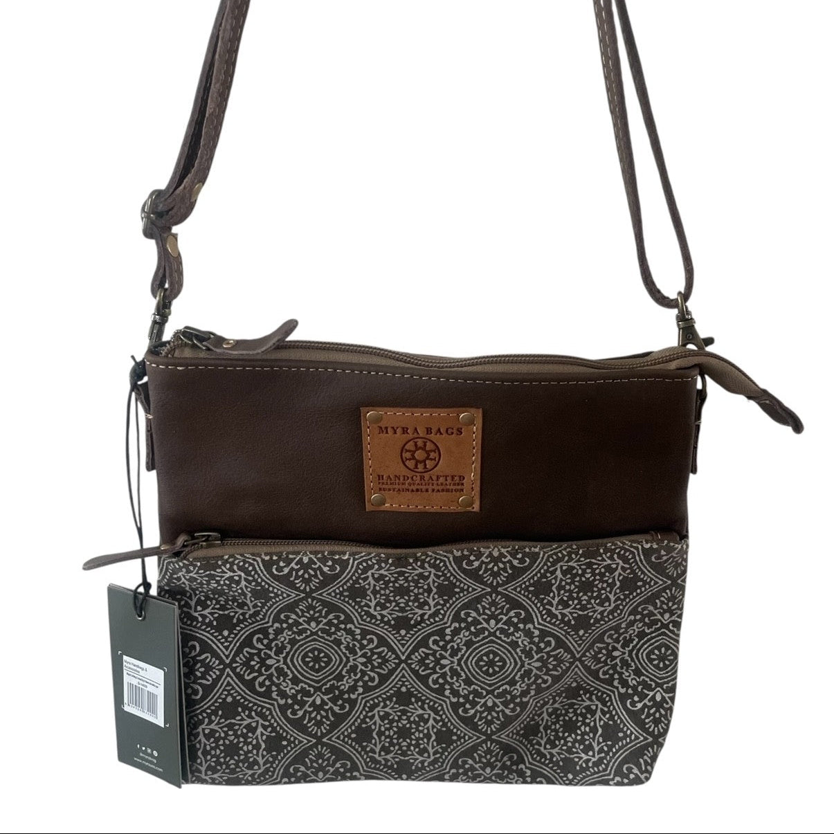 A women's crossbody bag by Stella Beach Manchester, featuring a dark brown leather top section with a tan brand patch, and a black and gray patterned fabric bottom section. It has a single shoulder strap and a hanging product tag.