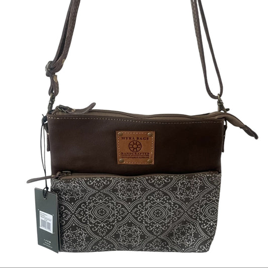 A women's crossbody bag by Stella Beach Manchester, featuring a dark brown leather top section with a tan brand patch, and a black and gray patterned fabric bottom section. It has a single shoulder strap and a hanging product tag.