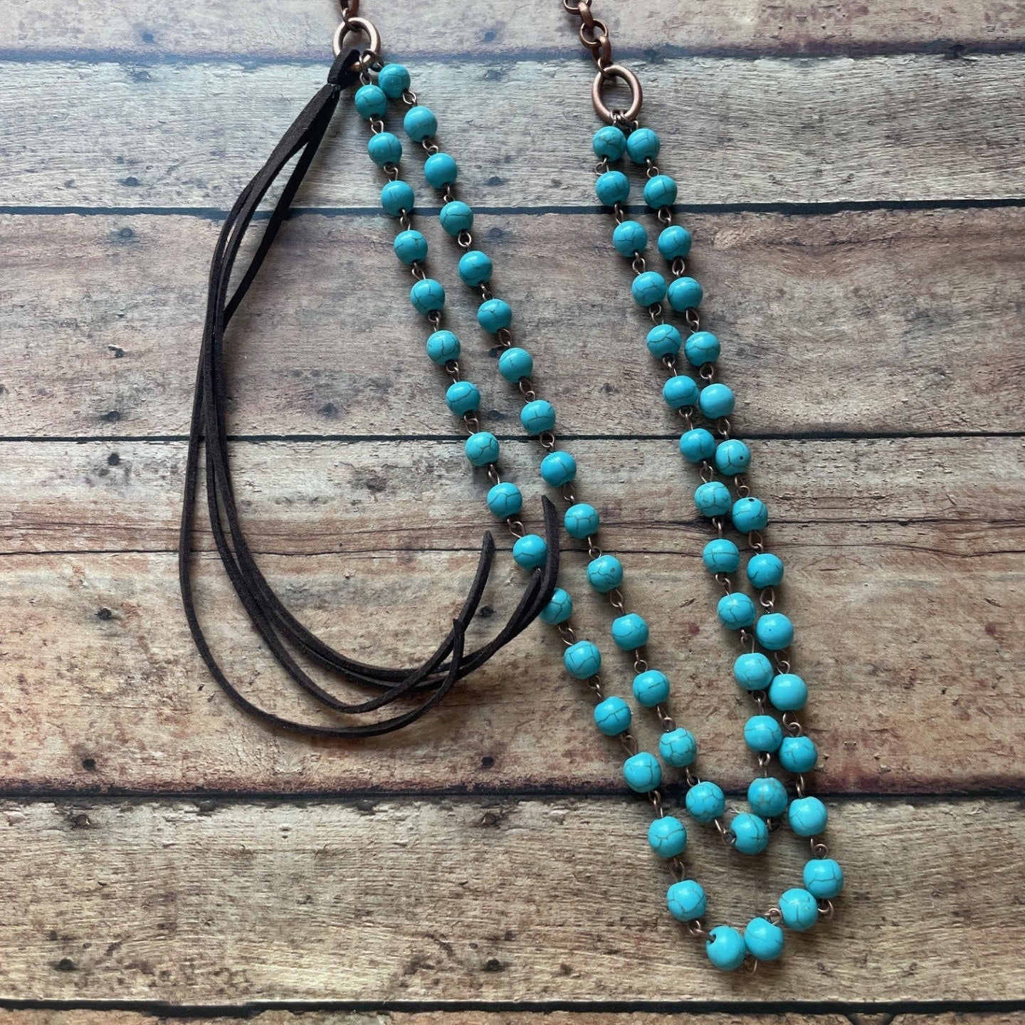 Turquoise beaded necklace with black cord on a wooden surface