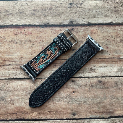Black leather watch strap with decorative metal buckle on a wooden surface