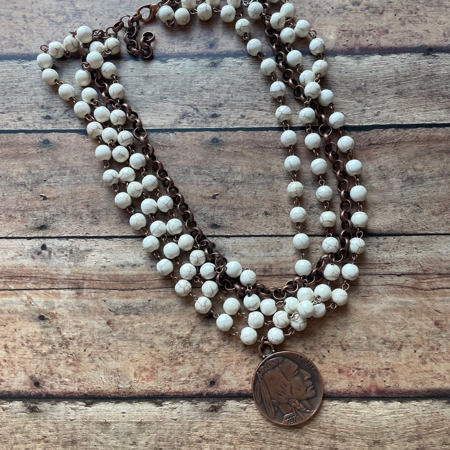 Necklace with white beads and brown chain on a wooden surface