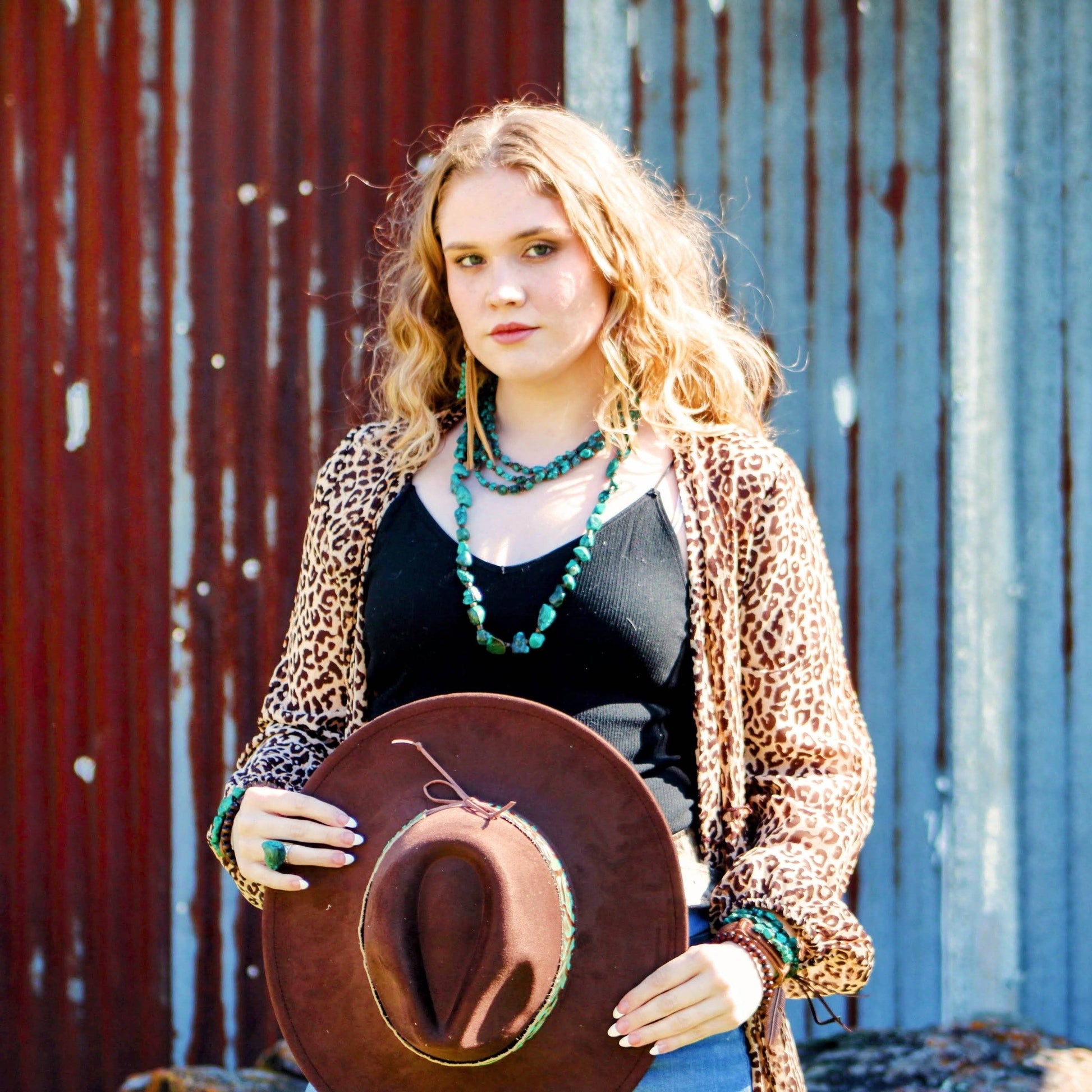 Woman holding a brown cowboy hat against a rustic metal wall.
