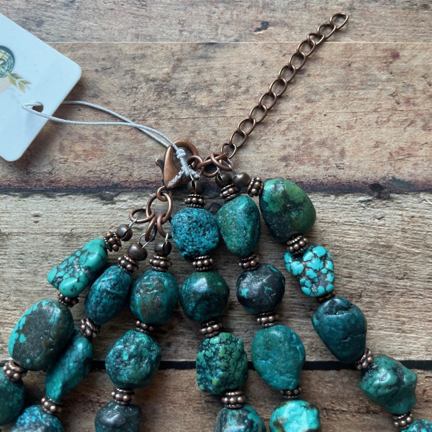 Turquoise beaded necklace with a tag on a wooden surface