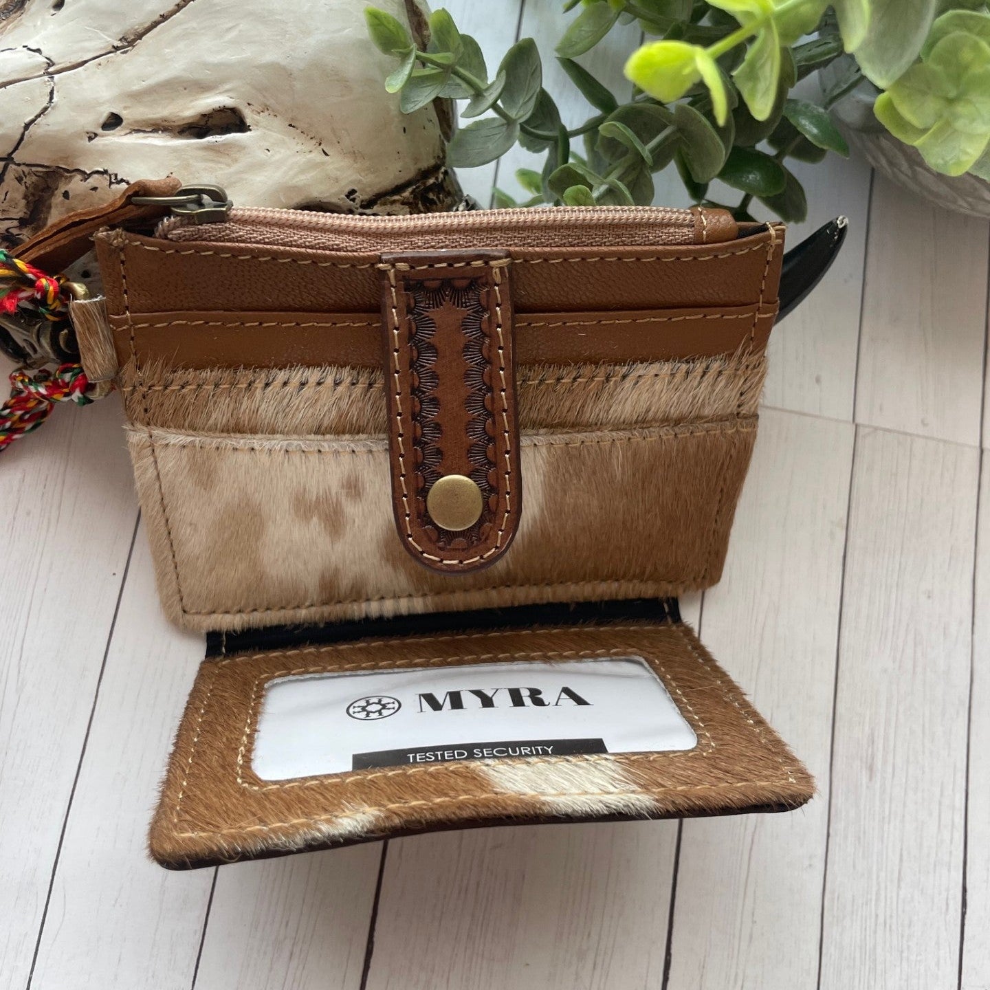 Brown leather wallet with the face head of a horse and a sunflower design on a wooden surface with plants in the background