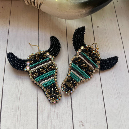 Decorative earrings with black, green, and gold beads on a wooden surface.