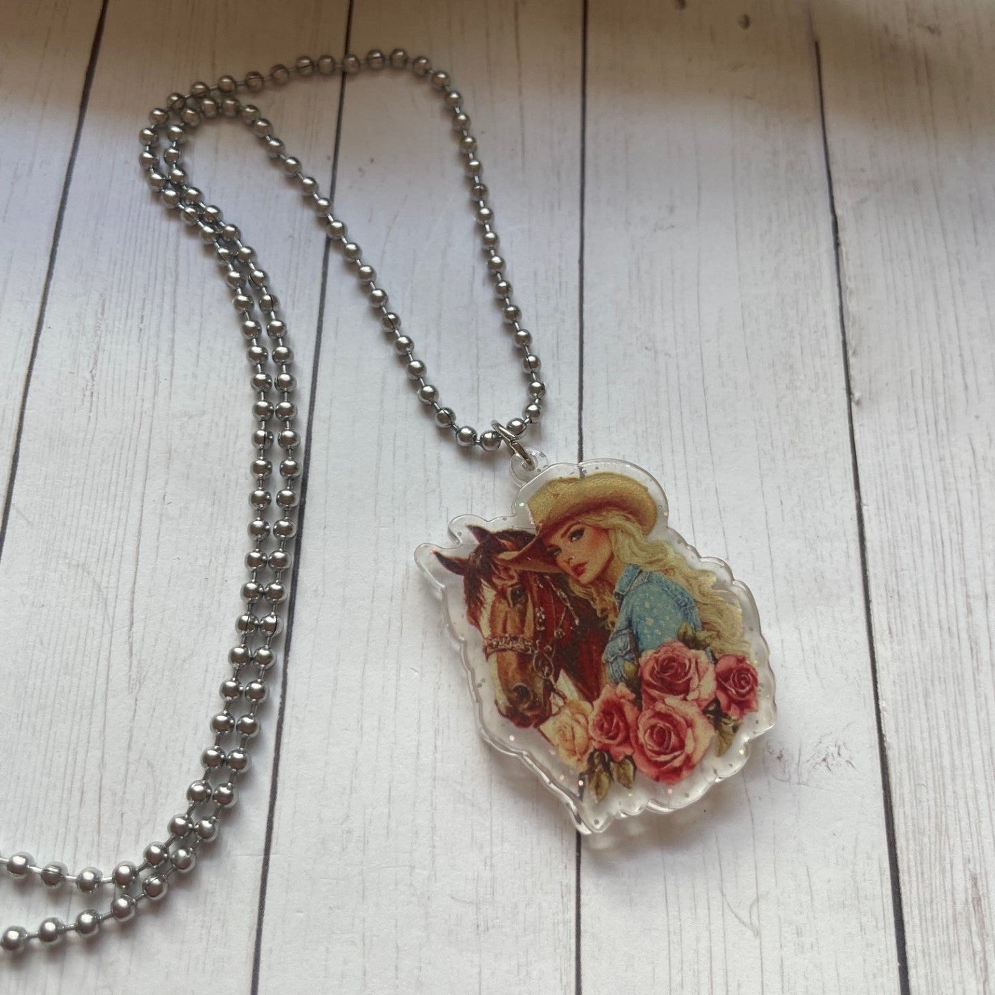 Necklace with a pendant featuring a girl and a horse on a wooden surface