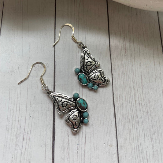 Butterfly-shaped earrings with turquoise stones on a wooden surface