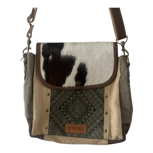 A crossbody handbag featuring a cowhide flap, beige canvas panels, a dark patterned textile panel, and brown leather trim, with a visible 'MYHA' brand patch on the front.